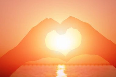 Güzel bir günbatımının arka planında ellerden yapılmış bir kalp