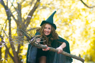 a witch on a broomstick among the forest. Portrait of a cute girl. mischievous sorceress. sexy girl with a broom and a witch hood in a raincoat