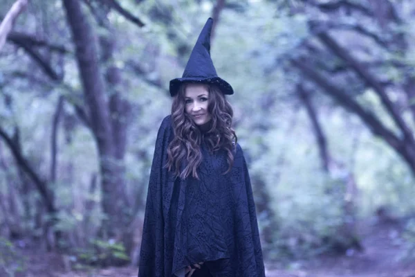 a witch in a hood and a cloak in the forest. Portrait of a cute girl. learning magic. school of magic. student magician