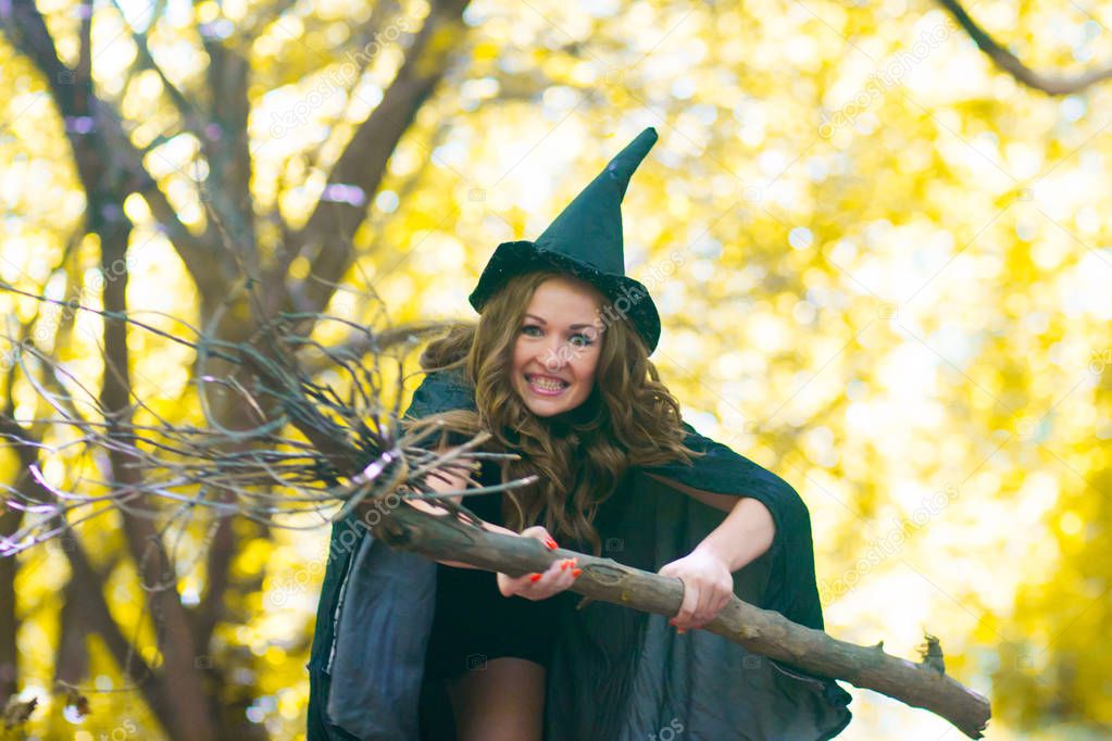 a witch on a broomstick among the forest. Portrait of a cute girl. mischievous sorceress. sexy girl with a broom and a witch hood in a raincoat