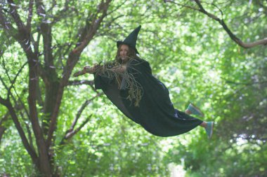 Cadının süpürgesi üzerinde uçan bir cadı. Çekici Cadılar Bayramı Kızı. orman arasında sinekler