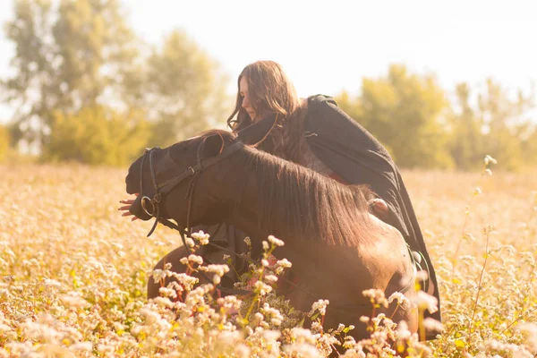 a girl riding a horse drives him on the field of buckwheat. beautiful girl in a raincoat