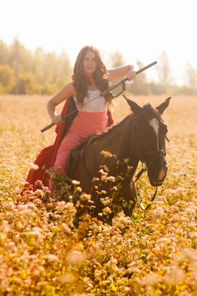 woman-warrior. beautiful girl on a black horse with a sword in her hands. among the grass and buckwheat field