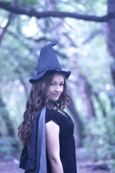 万圣节 女巫肖像 在森林里戴帽子和黑色斗篷的迷人女孩 纸张的垂直方向 — 图库照片