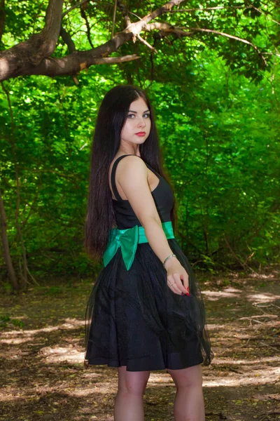 Linda morena em um vestido azul posando contra o pano de fundo da floresta . — Fotografia de Stock