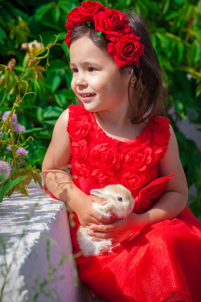 Uma linda menina em um vestido vermelho segurando um coelho . — Fotografia de Stock