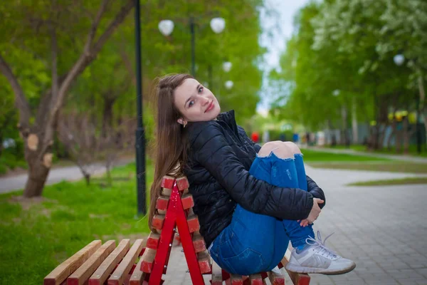 Uma linda garota está sentada em um banco. Mulher encantadora posando no parque . — Fotografia de Stock