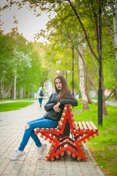 Молода красива дівчина сидить на лавці в парку . — стокове фото