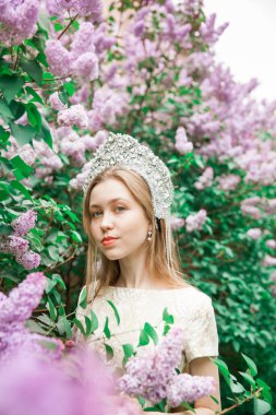 Tacın içindeki kız. Çiçek açan leylakların arasındaki peri masalından muhteşem kraliçe. Gümüş bir taç takmış, uzun saçlı güzel bir sarışın.