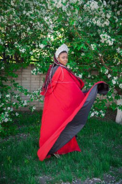 Kraliçe tacı ve kraliyet pelerini. Çiçek açan bir bahçenin arka planında güzel bir kız. Kırmızılı Afrikalı Amerikalı