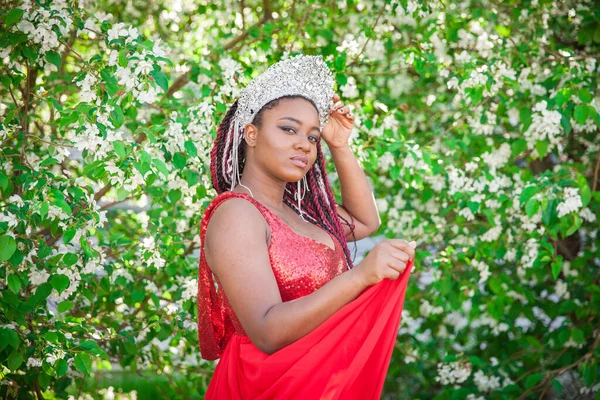 王冠と王室のマントルの女王 満開の庭を背景に素敵な女の子 赤でアフリカ系アメリカ人 — ストック写真