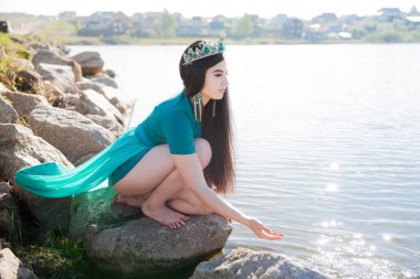 Yeşil elbiseli, trenli ve zümrüt renkli bir kraliçe. Gölde seksi bir esmer. Taşların üstünde kurbağalı bir kız. Peri doğası