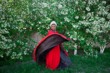 Kraliçe tacı ve kraliyet pelerini. Çiçek açan bir bahçenin arka planında güzel bir kız. Kırmızılı Afrikalı Amerikalı