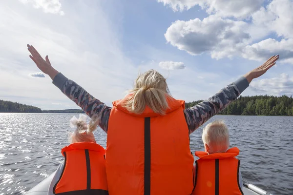Girl in a life jacket floating on the boat with his hands up. Children in life jackets sitting next
