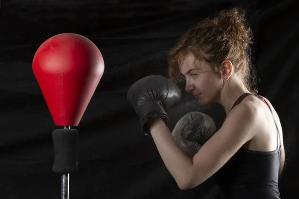 Young woman with boxing gloves and standing in position, ready to fight, copy space. Studio shot on black background, low key. Kickboxing and fight sport concept