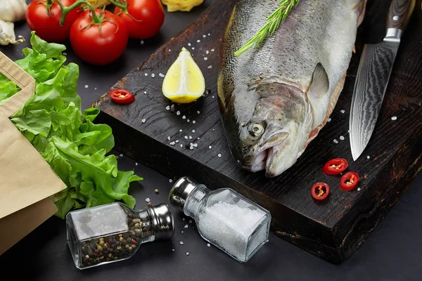 Fish with ingredients - healthy food, diet or cooking concept. Whole raw fish on dark vintage texture. Food background, top view, flat lay style.