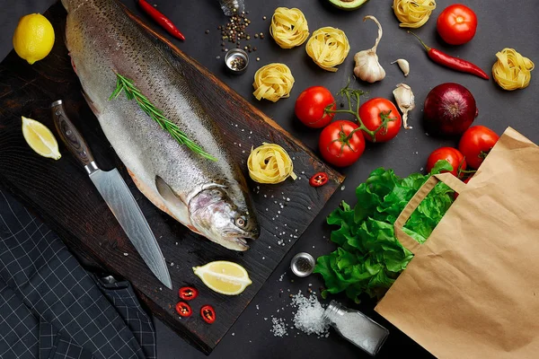 Fish with ingredients - healthy food, diet or cooking concept. Whole raw fish on dark vintage texture. Food background, top view, flat lay style.