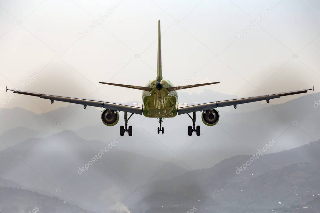 Aircraft, airliner with landing gear comes to land on the background of the mountains. Rear view.