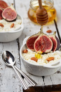 İncir, bal ve badem hafif bir arka plan üzerinde beyaz bir kase süzme peynir. Konsept: sağlıklı kahvaltı