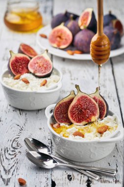 İncir, bal ve badem hafif bir arka plan üzerinde beyaz bir kase süzme peynir. Konsept: sağlıklı kahvaltı