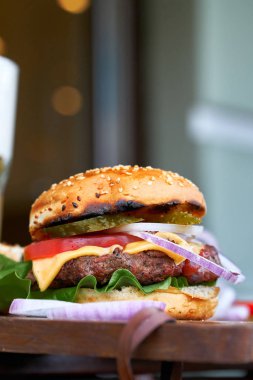 Biftek, soğan, domates, marul ve peynirli ev yapımı hamburger.