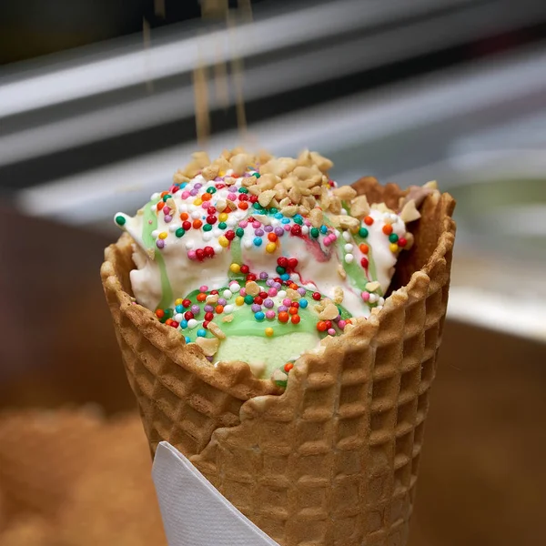 white ice cream in a waffle cone with colored sprinkles and falling pieces of nuts