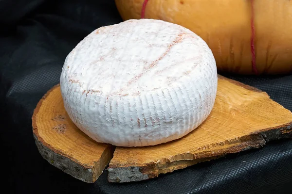 Big head of cheese in a white mold lying on a wooden board, black backgraund
