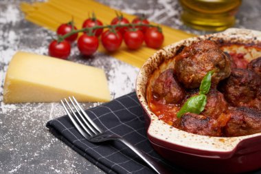 Masada köfte ve domates soslu seramik güveç çanak. yemeğin yanında domates, makarna, peynir, çatal vardır