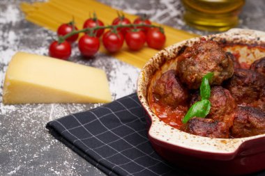 domates soslu köfte ve fesleğen yaprağı ile dekore edilmiş, gri arka plan üzerinde beyaz ve kırmızı tavada servis edilir. taze domates, spagetti ve sert peynir bir parça yakın tava yanında. Closeup.