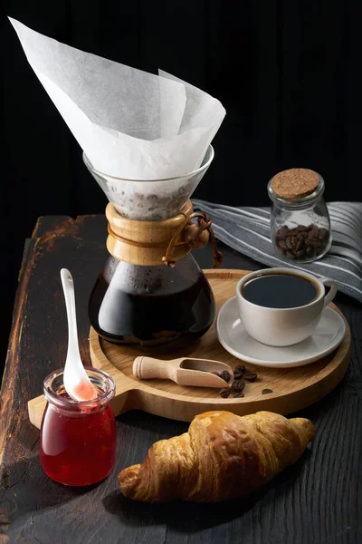 Pour over coffee brewing method. Making pour over coffee with hot water being poured from a kettle. a jug for pouring over coffee, a cup of coffee on a light wooden round tray, jam in a jar, coffee gr