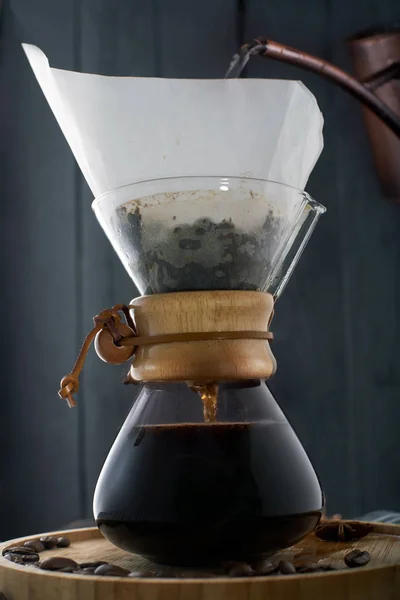Coffee pouring into a glass coffee maker. Pour Over Coffee in a decanter, a carafe for coffee on a white coffee set background, coffee beans, light wooden tray, dark background, close up