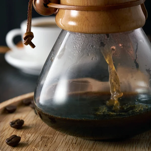 Café versé dans une cafetière en verre. Verser sur le café dans une carafe, une carafe pour le café sur un fond de café blanc, grains de café, plateau en bois clair, fond sombre, gros plan — Photo