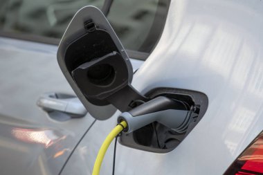 Elektrikli araba gümüş rengi, şarj için fişe takılmış. Elektrikli araba şarj istasyonu. Şarj olan bir elektrikli arabaya takılan güç kaynağını kapatın. Araba şarj kablosu.