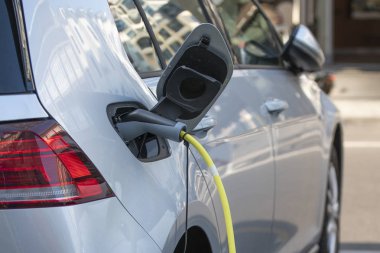 Elektrikli araba gümüş rengi, şarj için fişe takılmış. Elektrikli araba şarj istasyonu. Şarj olan bir elektrikli arabaya takılan güç kaynağını kapatın. Araba şarj kablosu.