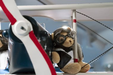 Eski bir uçağın kanadında pilot gözlüğü ve pilot ceketi takan oyuncak ayı. Kapat..