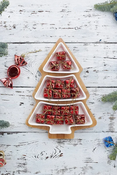 Lots of little red gift boxes in a Christmas tree shaped plate on a white background. Top view. vertical frame. the concept of Christmas composition — Stock Photo, Image