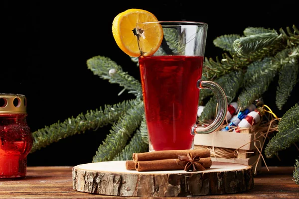 Christmas mulled wine red in a glass with a stick of cinnamon and a piece of orange on the background of a tree branch. wooden background — Stock Photo, Image