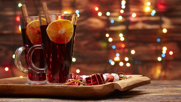 Weihnachtsglühwein rot im Glas mit einer Stange Zimt und einem Stück Orange auf einem Hintergrund aus glitzernden Lichtern — Stockfoto