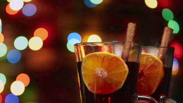 Рождественское глинтвейн красный в стакане с палкой корицы и кусок апельсина на фоне мерцающих огней — стоковое фото