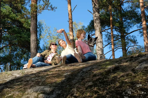 Young female friends enjoying nature, sitting on a rock with dog and making selfies on nature. The concept of the blog — Stock Photo, Image