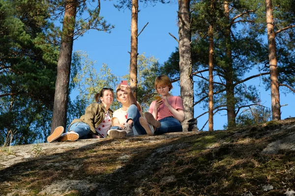 Jóvenes amigas disfrutando de la naturaleza, sentadas en una roca y tomando selfies en la naturaleza. El concepto del blog Fotos de stock