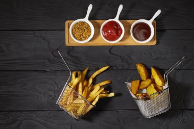 Patates kızartması ve patates kızartması ve üç farklı sos: ketçap, hardal ve barbekü koyu arka planda, üst manzara, yatay fotoğraf.
