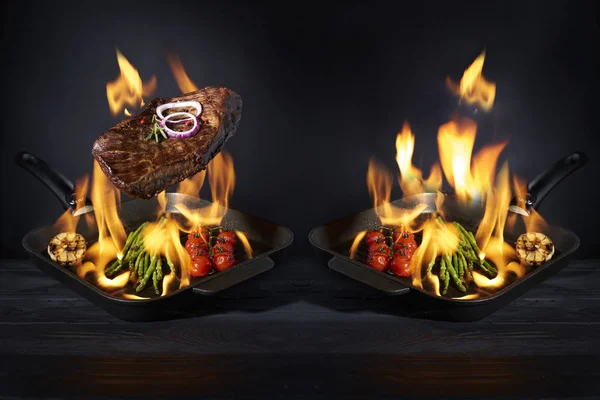 Προετοιμασία μπριζόλα και λαχανικά σε τηγάνι με φωτιά φλόγα σε σκούρο φόντο. Εστιατόριο και υπηρεσία ξενοδοχείου έννοια. Έννοια υπηρεσιών εστιατορίου και ξενοδοχείου. — Φωτογραφία Αρχείου