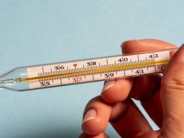 Elinde mavi bir arka planda cıva termometresi var. Yüksek ateş ve hastalık