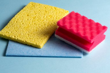 Mavi arka planda farklı renk ve boyutlarda temizlik süngerlerinin yan görünüşü. Ev temizlik ürünleri