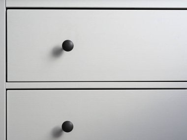 Siyah saplı çekmecelerden oluşan modern beyaz tahta bir sandığa yakın plan. Minimalizm, modern iç mekan