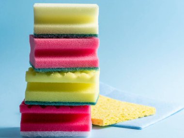 Mavi arka planda farklı renk ve boyutlarda temizlik süngerlerinin yan görünüşü. Ev temizlik ürünleri