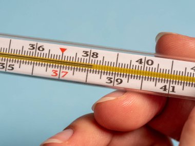 Mavi arka planda izole edilmiş bir kadının elindeki cıva termometre. Termometre kullanarak sıcaklık ölçümü. Yüksek ateş ve hastalık. Kapat.