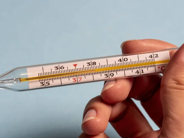 mercury thermometer in the hand of a woman isolated on a blue background. Temperature measurement using a thermometer. High fever and illness