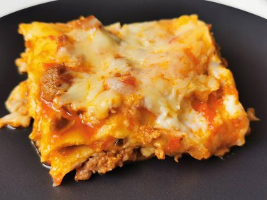 Bir parça ev yapımı lazanya siyah bir tabakta duruyor. Hamur katmanları ve Bechamel soslu İtalyan yemeği.
